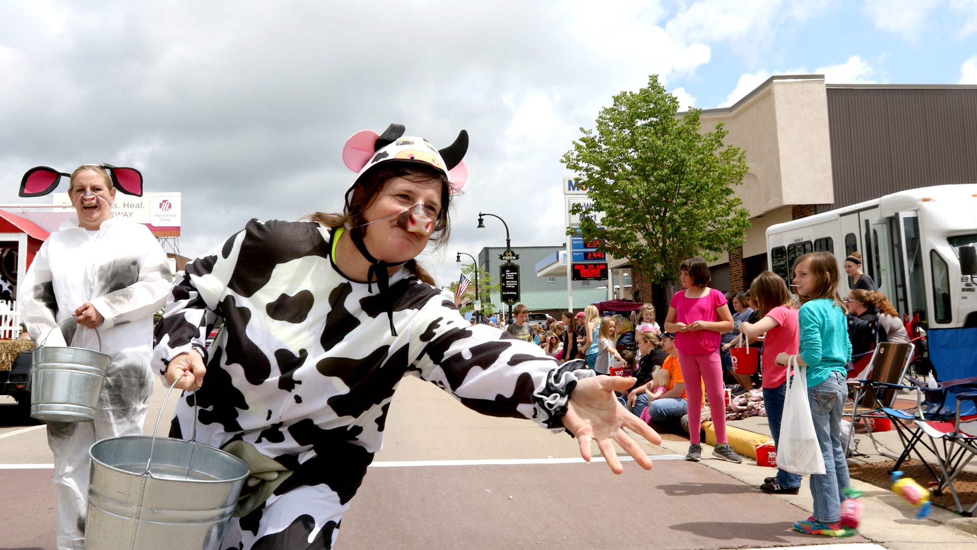 Person dressed as cow throwing candy to kids during a parade